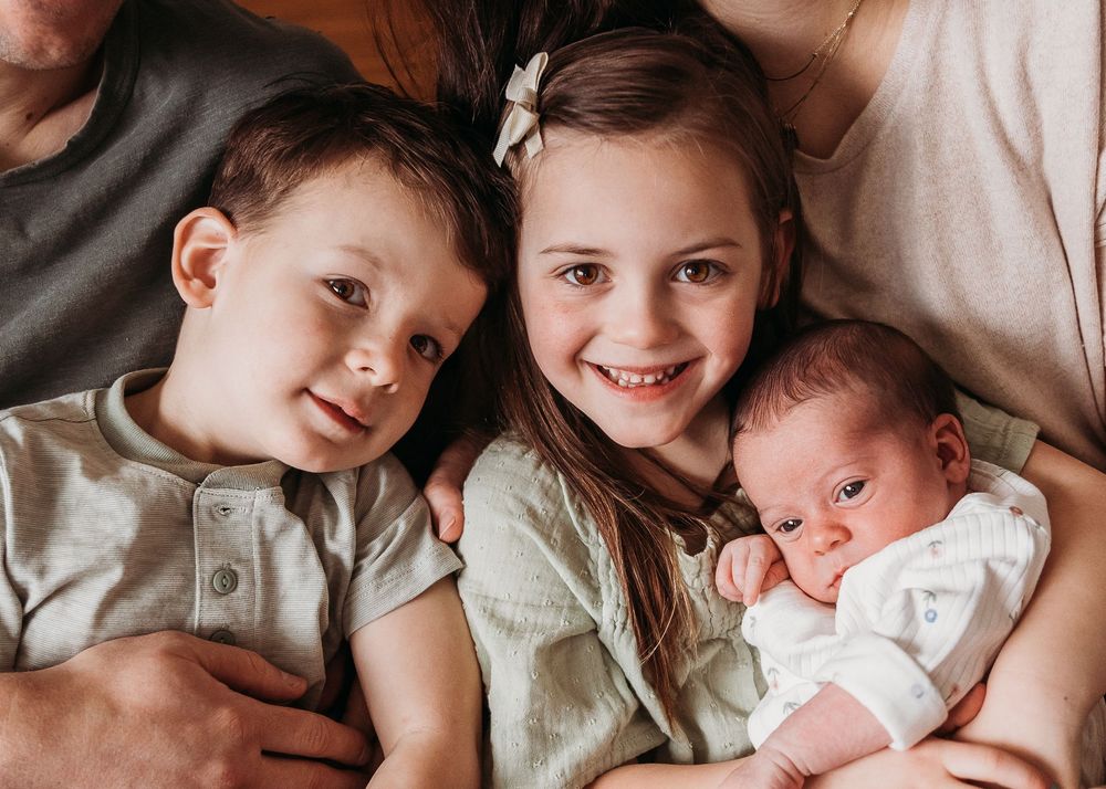 Three siblings cuddled together in a tender family portrait, with newborn in white onesie.