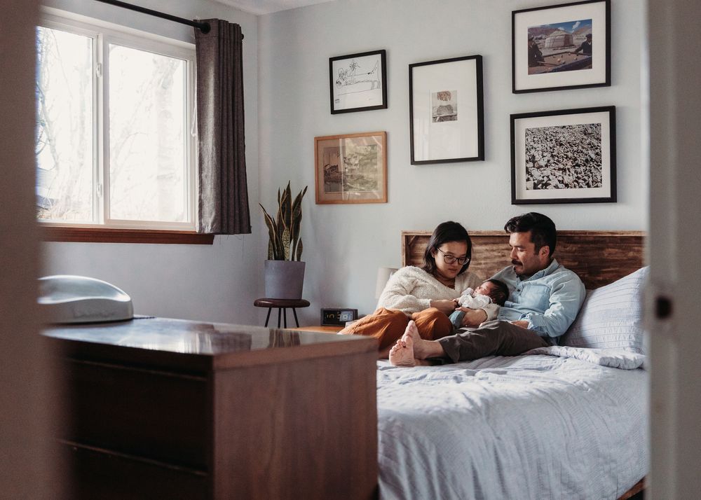 People relax together on a bed in a cozy bedroom with framed artwork on the light gray walls.
