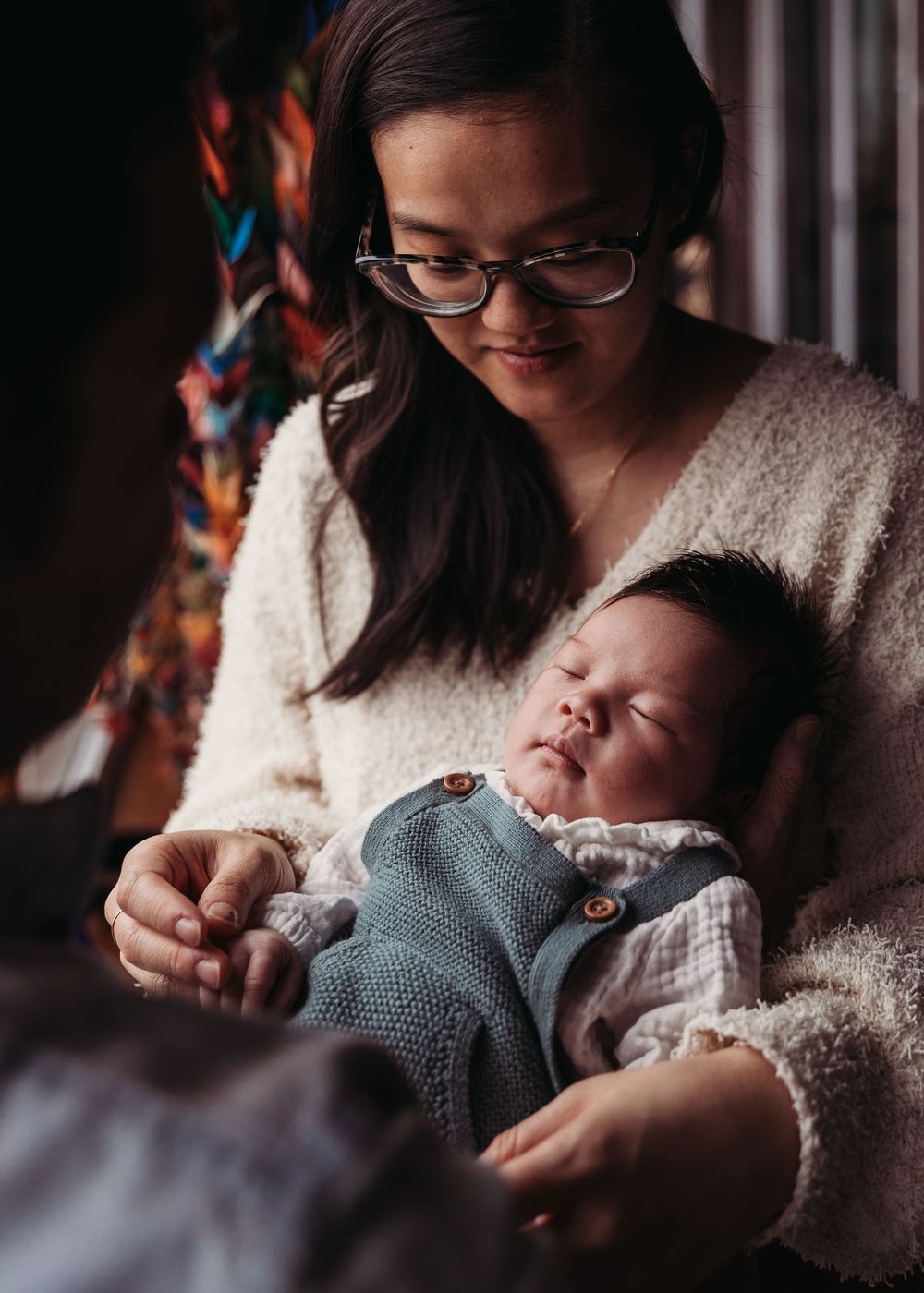 A sleeping baby in a knit sweater rests peacefully in a caregiver's arms.