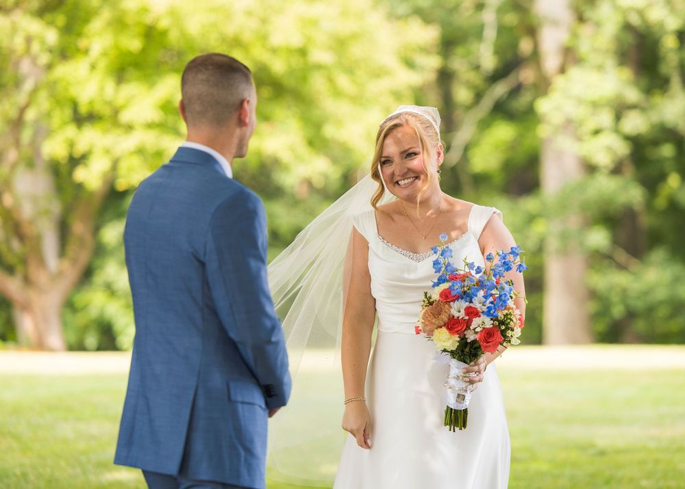 Wedding party poses for outdoor portraits in bright natural setting with white dress and blue suits.