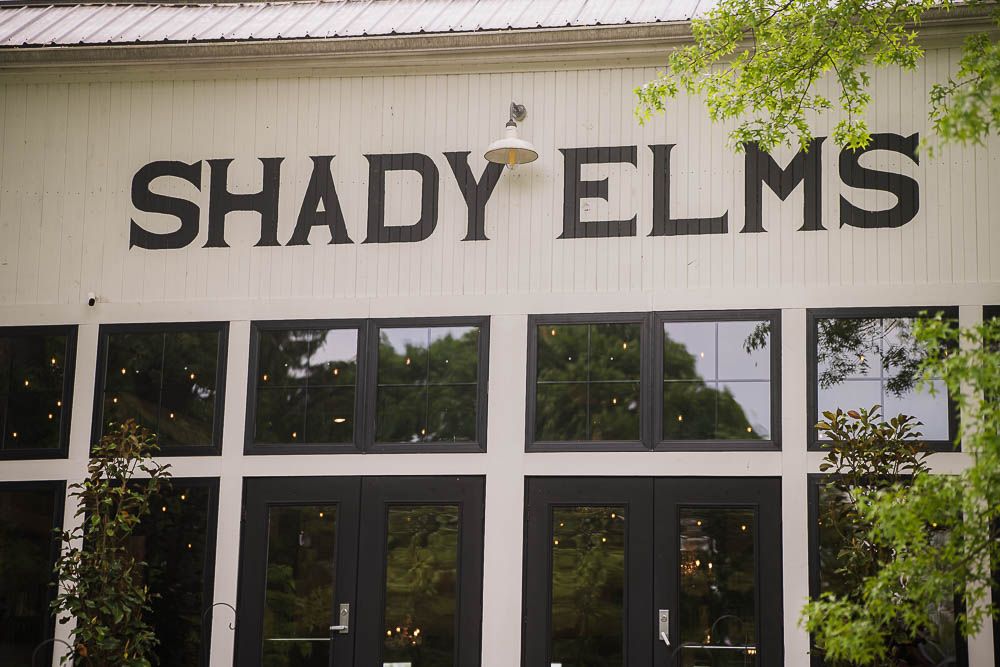 Shady Elms Farms Wedding Venue sign mounted on a white barn exterior with windows and green foliage above outside pittsburgh pa, photography