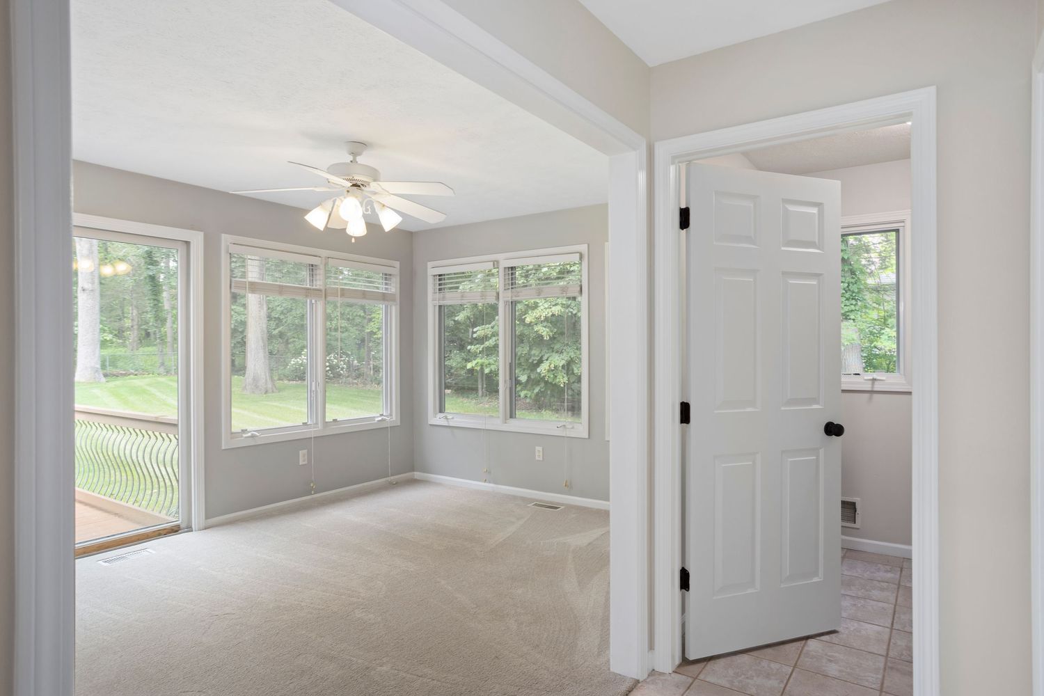 Sunroom with white trim, ceiling fan, and large windows providing panoramic views of the backyard.