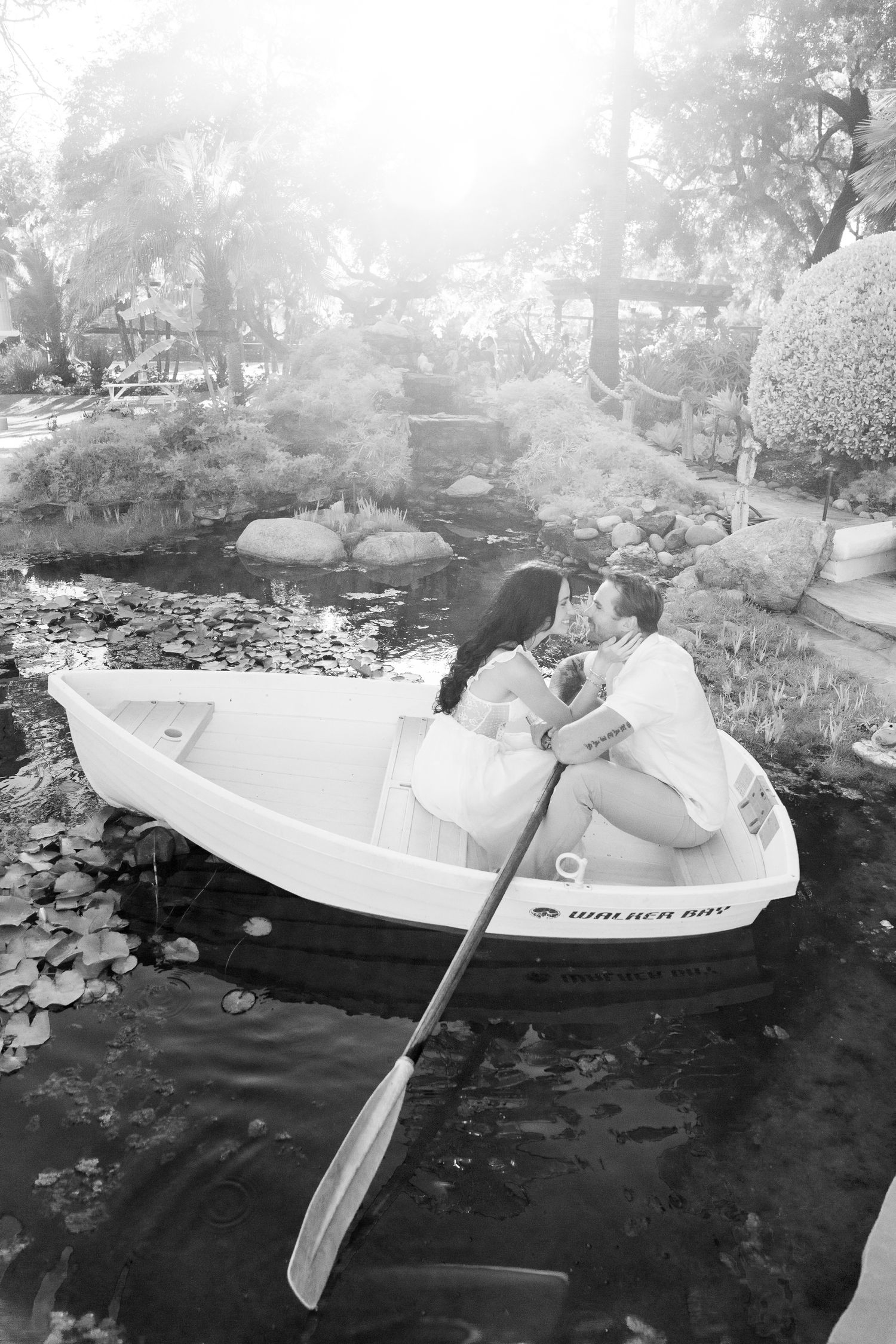 A romantic boat ride through a tranquil garden pond with lily pads, surrounded by misty landscaping and trees.
