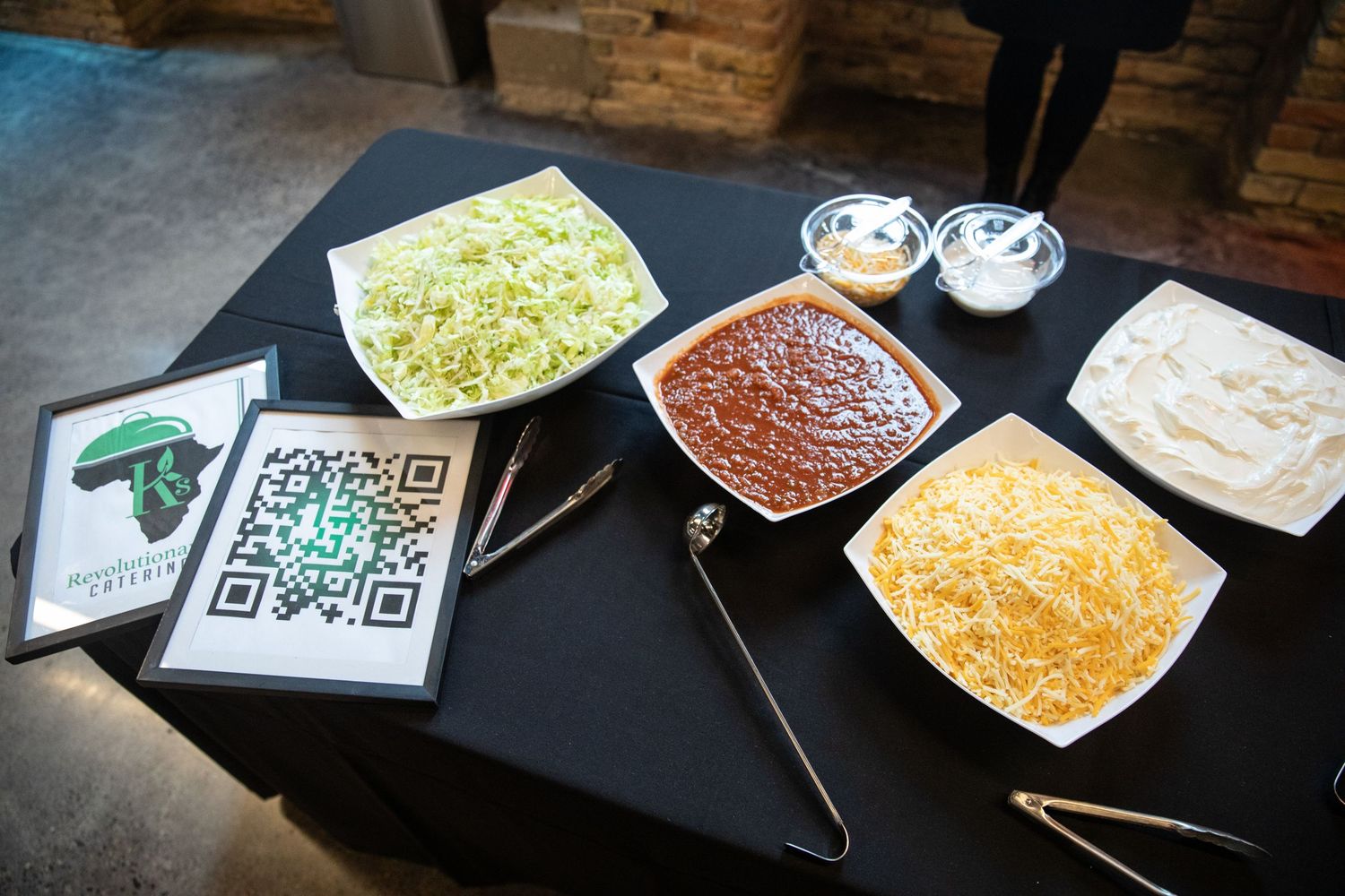 Various taco toppings including shredded cheese, beans, and lettuce arranged on plates alongside a QR code menu.