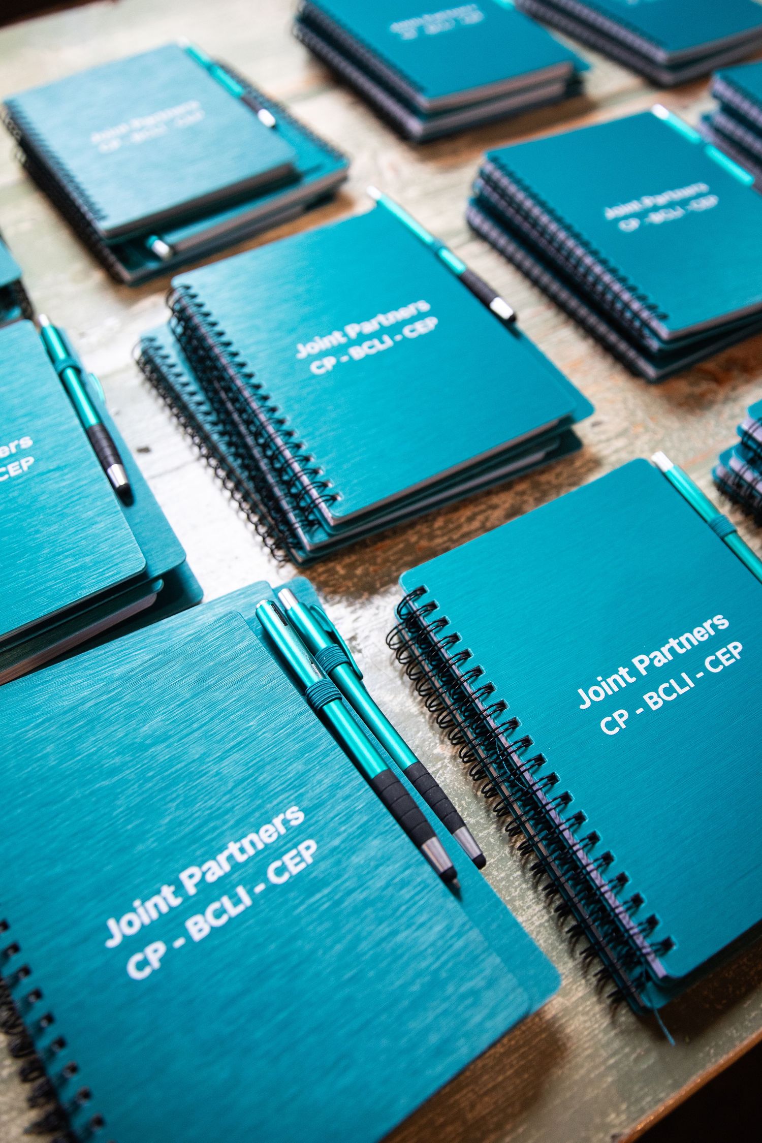 Multiple teal spiral notebooks with black pens laid out neatly on a wooden surface.