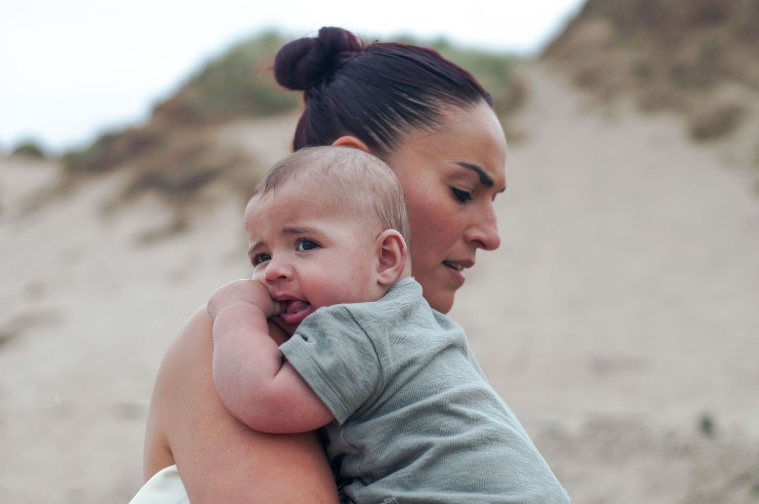 A caring moment shared between parent and child on a sandy beach with dunes in the background.
