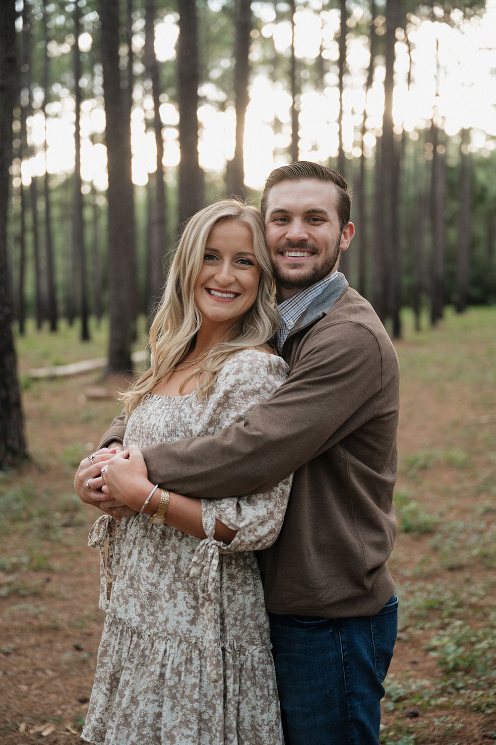 A loving couple embraces while smiling in a serene pine forest at golden hour.