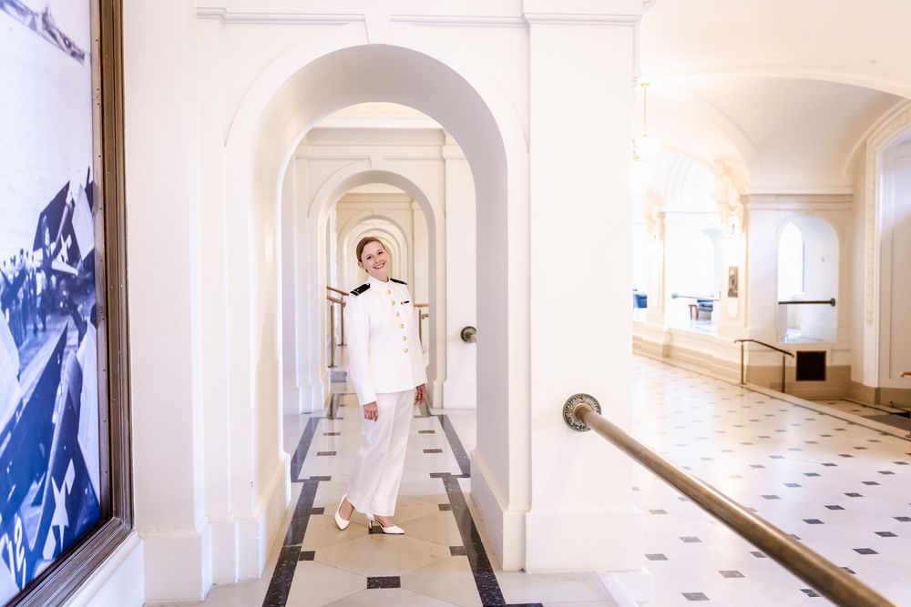 Person in white attire stands in long elegant arched hallway with tiled floors and handrails.
