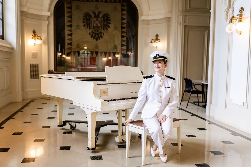Elegant white grand piano sits in a luxurious room with marble floors and ornate wall decor featuring a golden eagle crest.