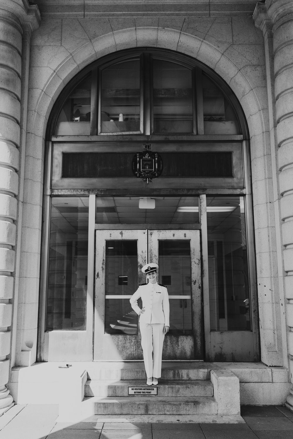 A uniformed service member stands in front of a grand arched entrance in a black and white photograph.