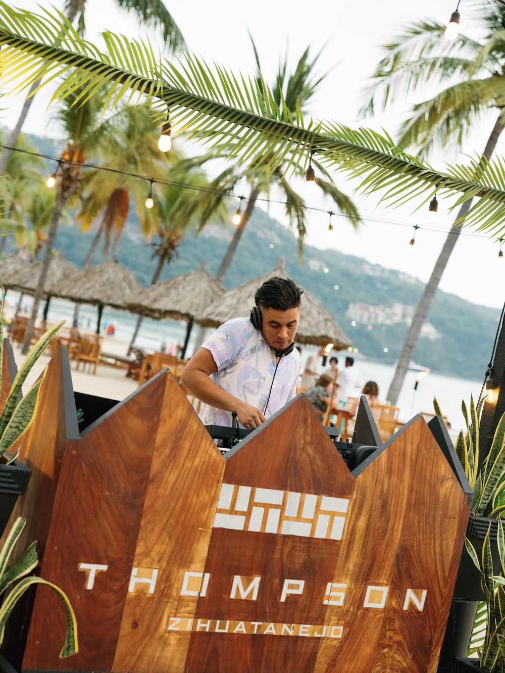 Wooden Thompson Huatanejo sign with palm trees and ocean view in background.