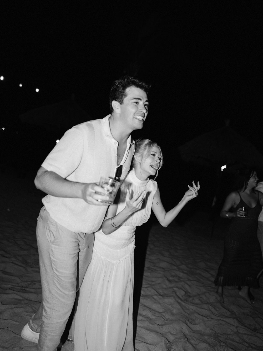 A couple dancing and laughing together on a sandy beach at night.