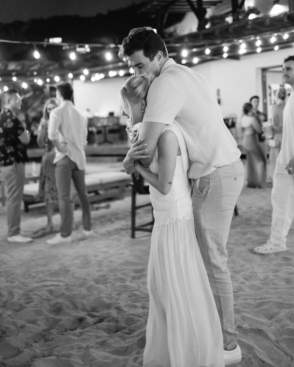 A couple sharing an intimate dance moment on a sandy beach under string lights.