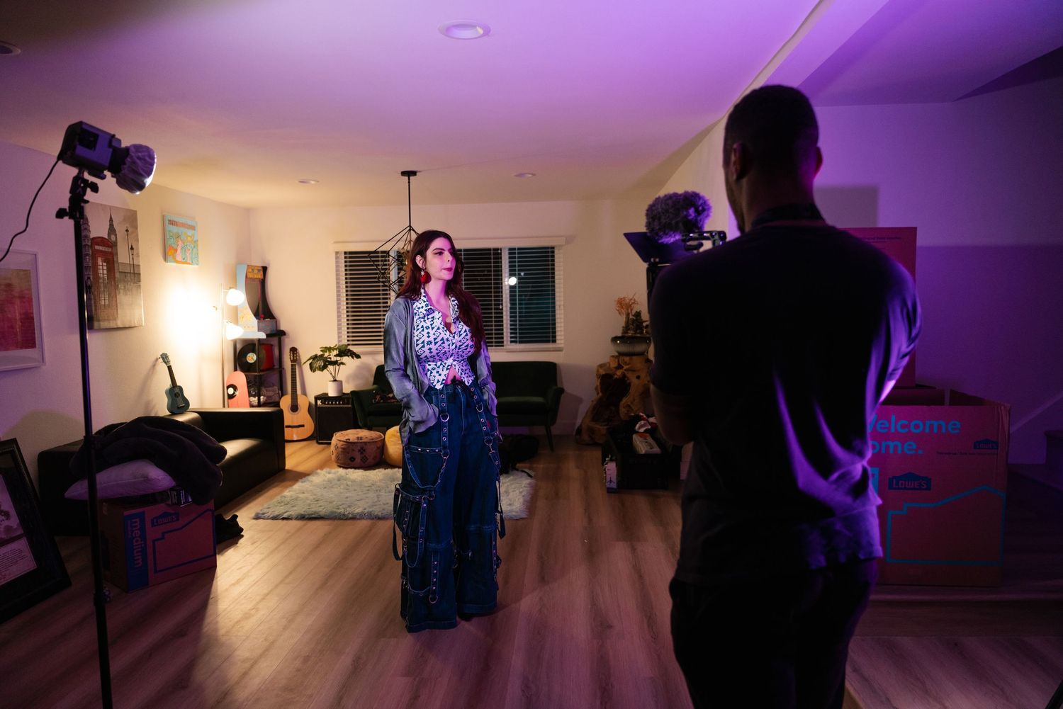 A film shoot in a living room with purple lighting as someone records a performer in an elegant blue dress.
