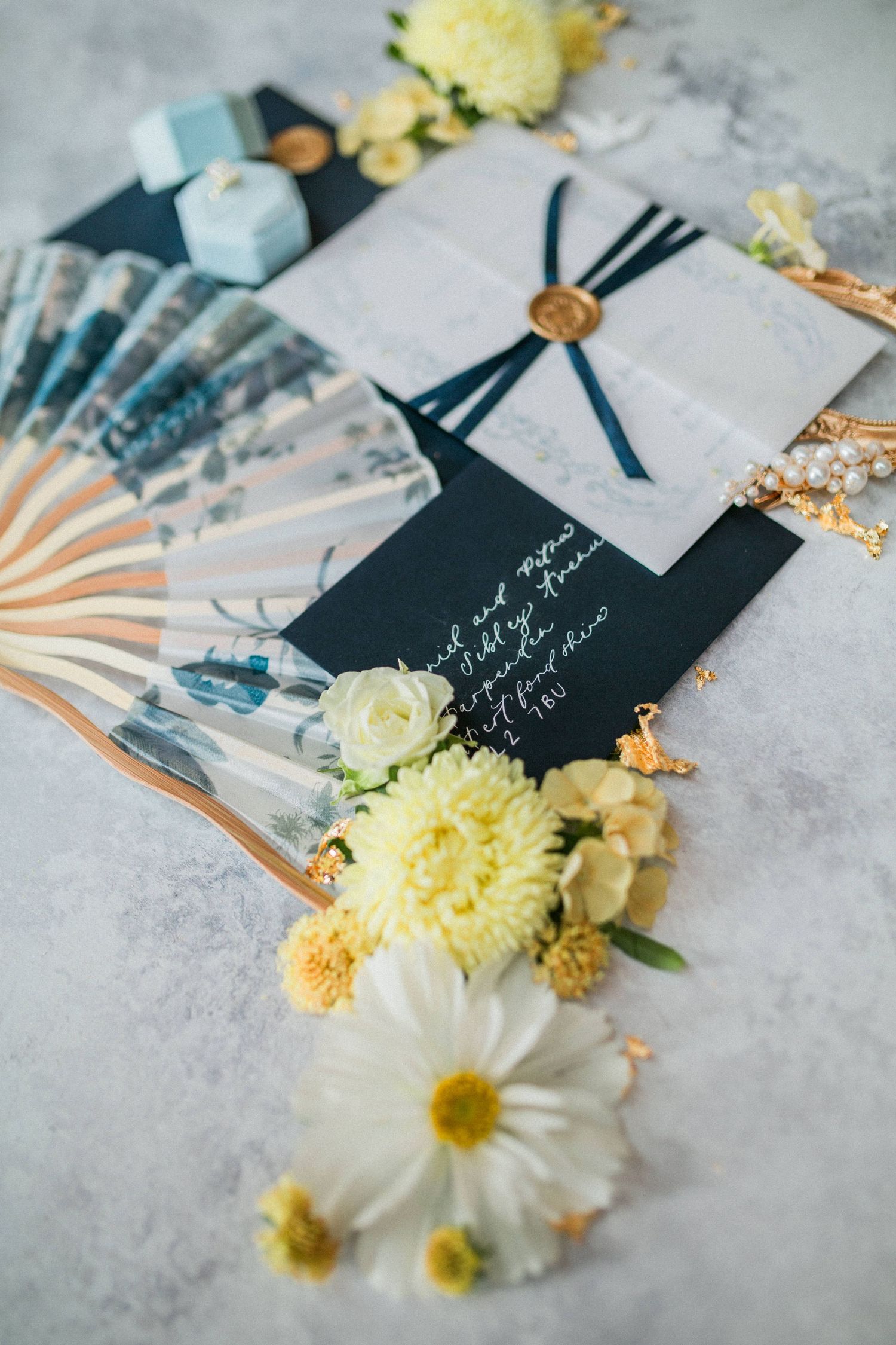 Wedding stationery flatlay with navy and white invitation, paper fan, and yellow and white flowers at Euridge - Hayley Elizabeth Photography