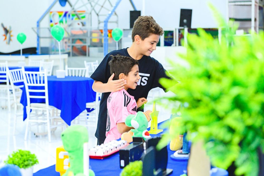 Two people are engaged in an activity at an outdoor event with blue chairs and green decor visible in the background.