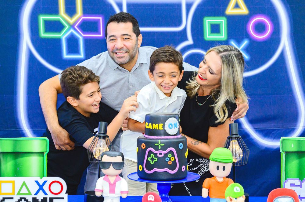 Happy family enjoying a gaming-themed party celebration with neon controller backdrop and colorful decorations.