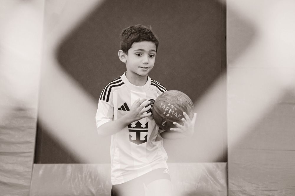 Young basketball player in an Adidas jersey holds a ball in black and white artistic sports portrait.