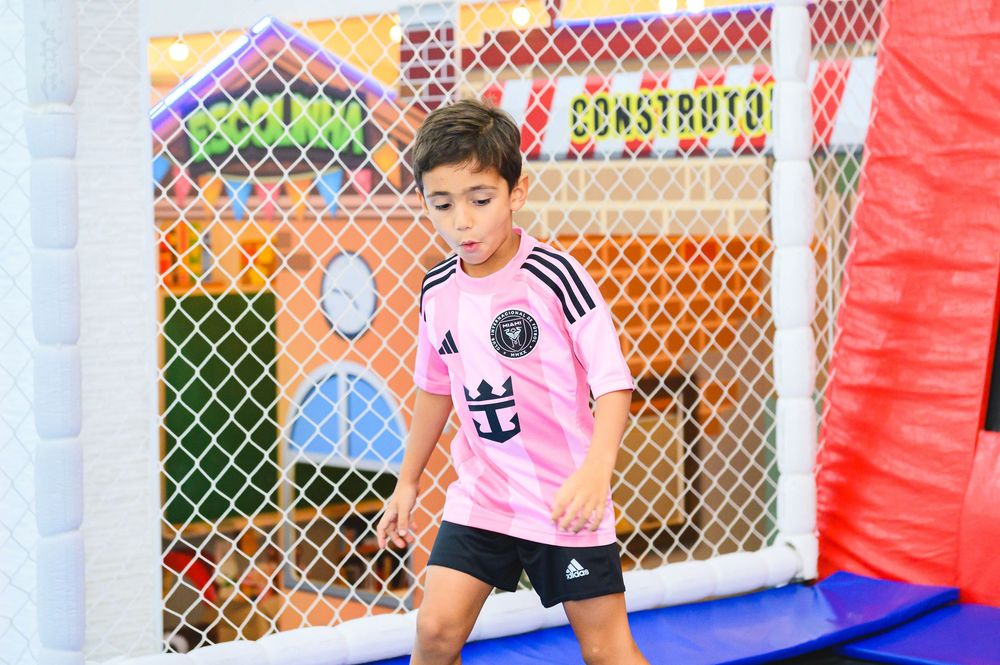A young player in a pink jersey enjoys playing on an inflatable sports game with safety netting in the background.