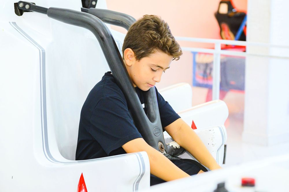 Young person in a navy shirt sits focused in a bright white exercise machine or equipment.