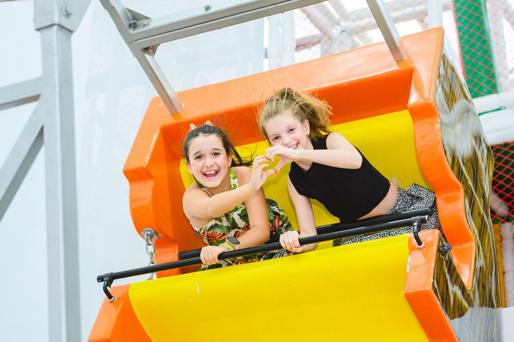 Two people enjoying a thrilling amusement park ride with colorful orange and yellow sections.