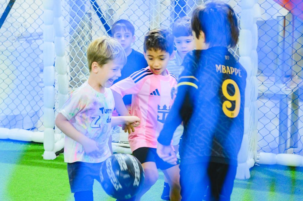 Children playing indoor soccer with coaches in colorful sports uniforms.