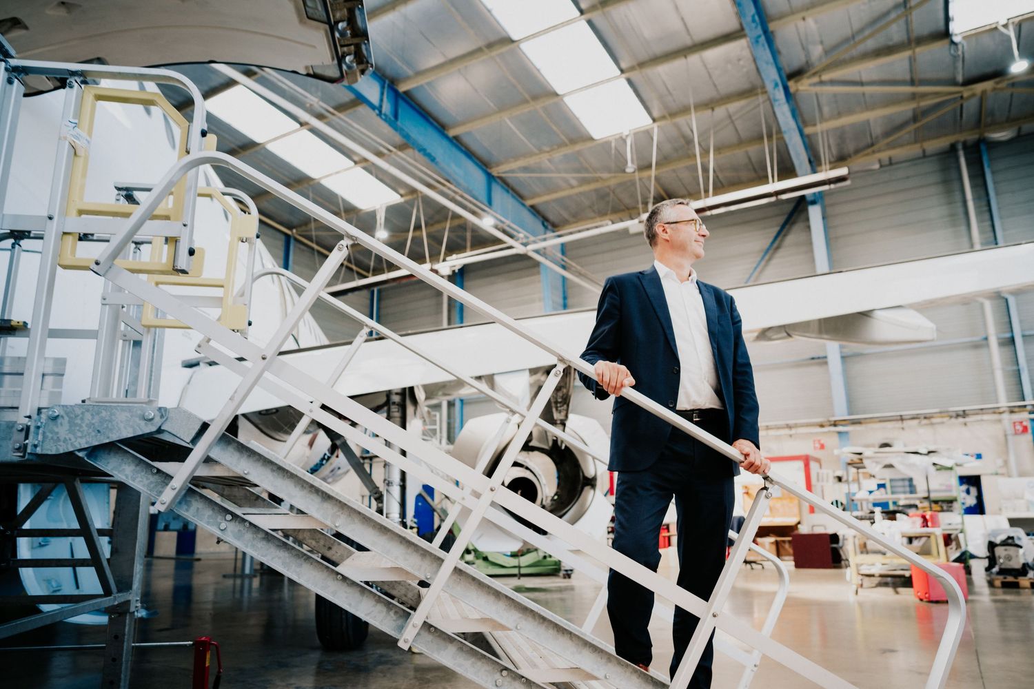 Photographe portrait toulouse. PDG sur un escalier blanc dans un espace de travail industriel avec des composants d'avion.