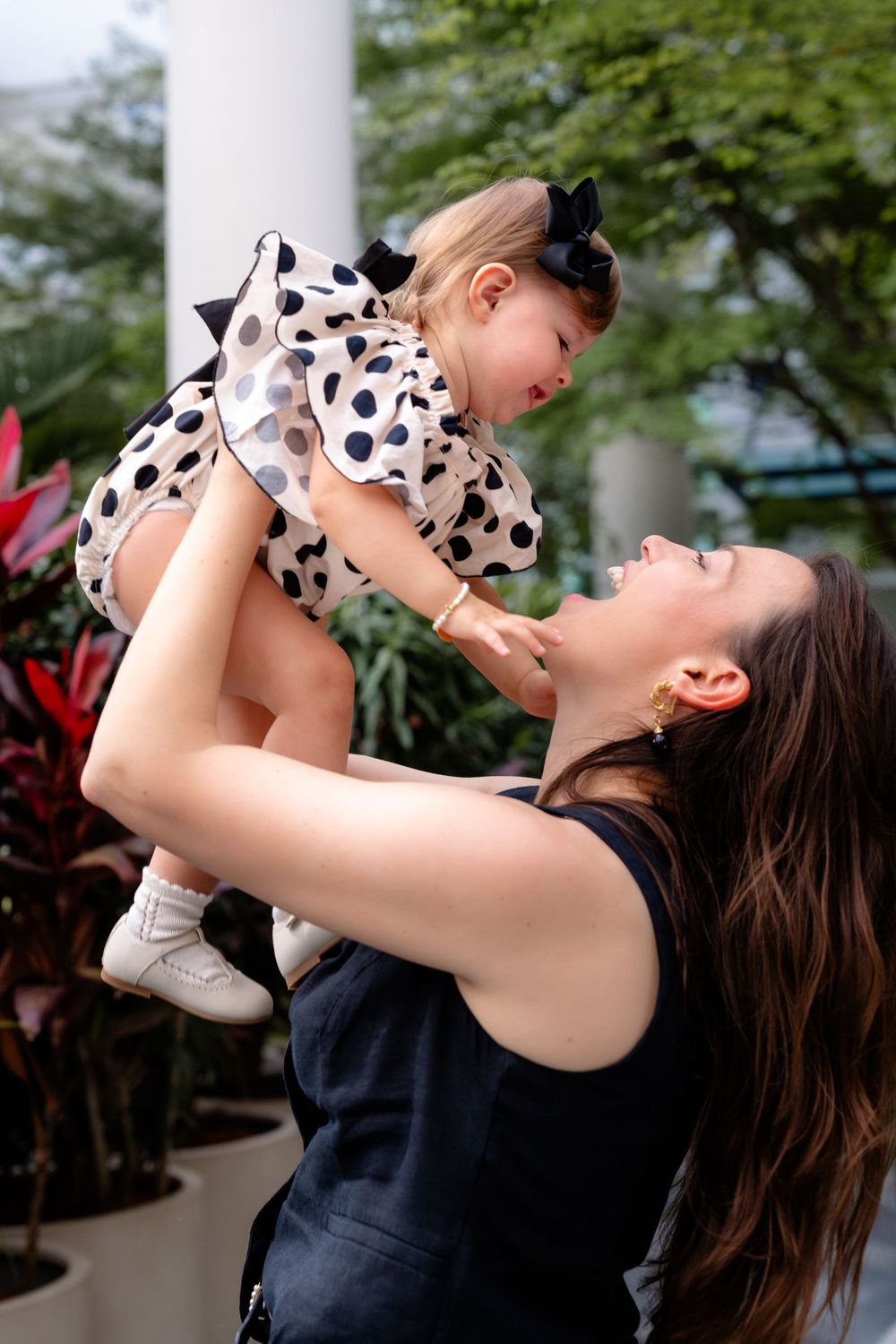 A person holds up a small child wearing a polka dot dress, sharing a joyful moment together outdoors.