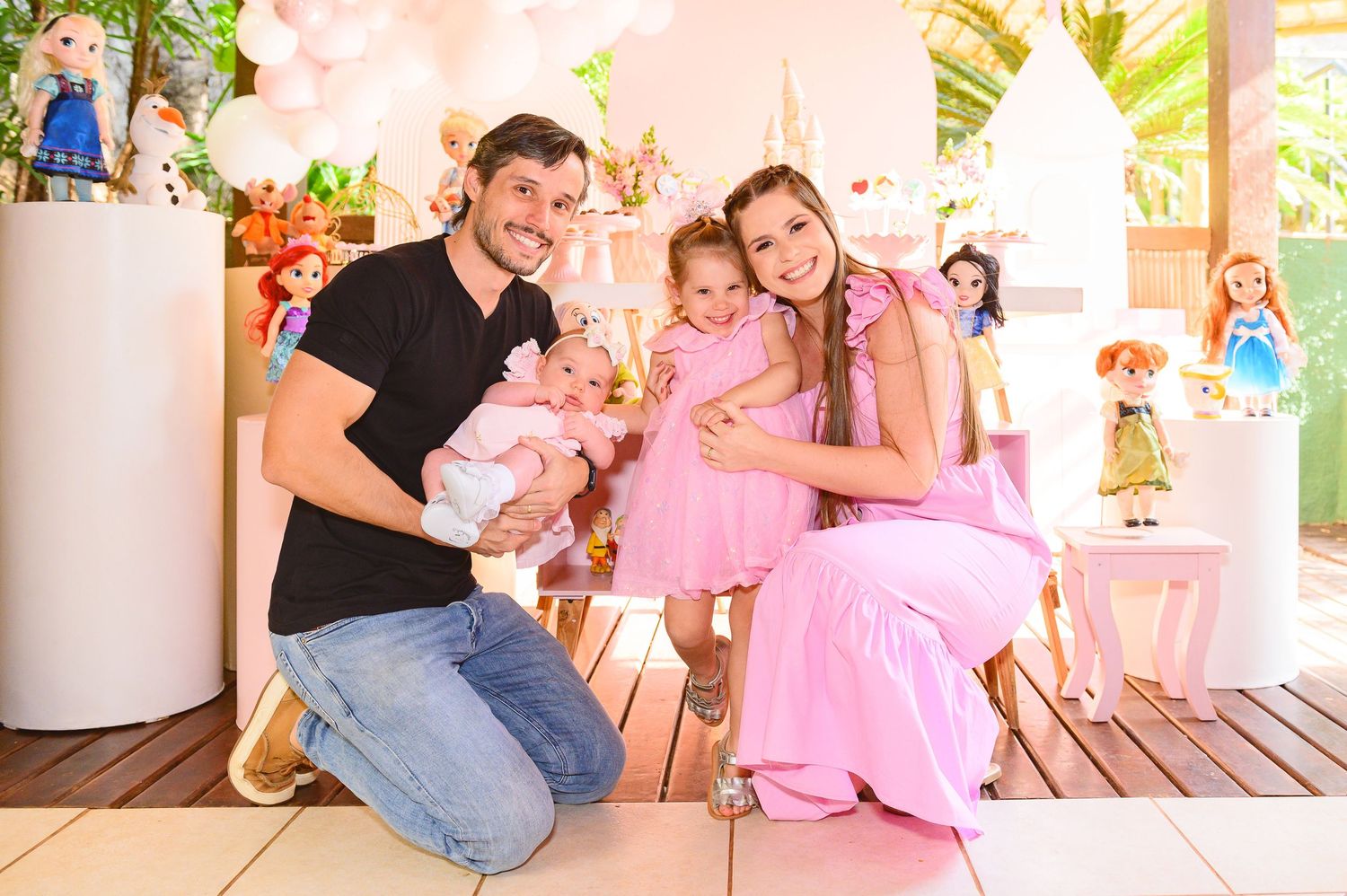 A joyful family gathering at a pink-themed party with dolls and decorative displays in the background.