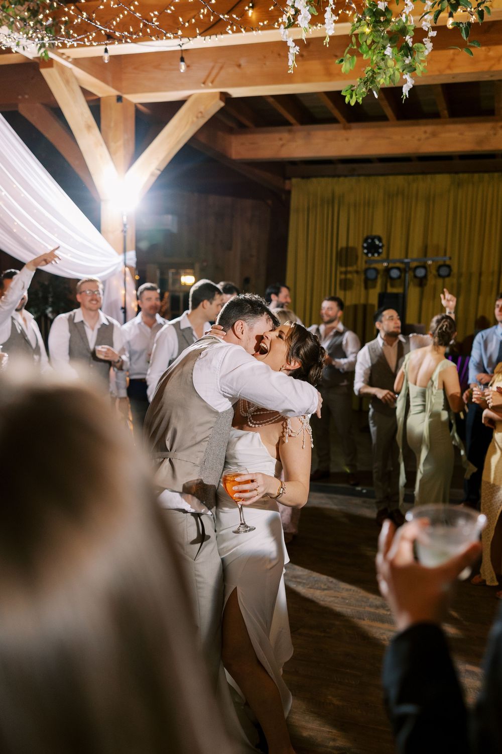 A romantic first dance between a newlywed couple under wooden beams adorned with string lights during their barn reception at Windham Manor.