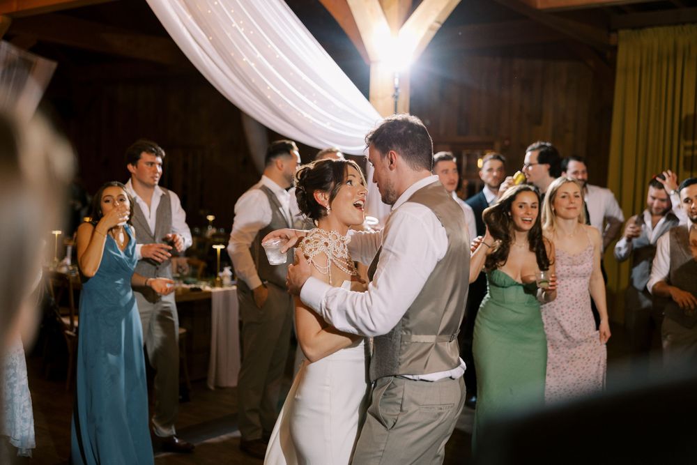 Newlyweds share their first dance at a rustic wedding reception under draped fabric decor while guests look on at Windham Manor.
