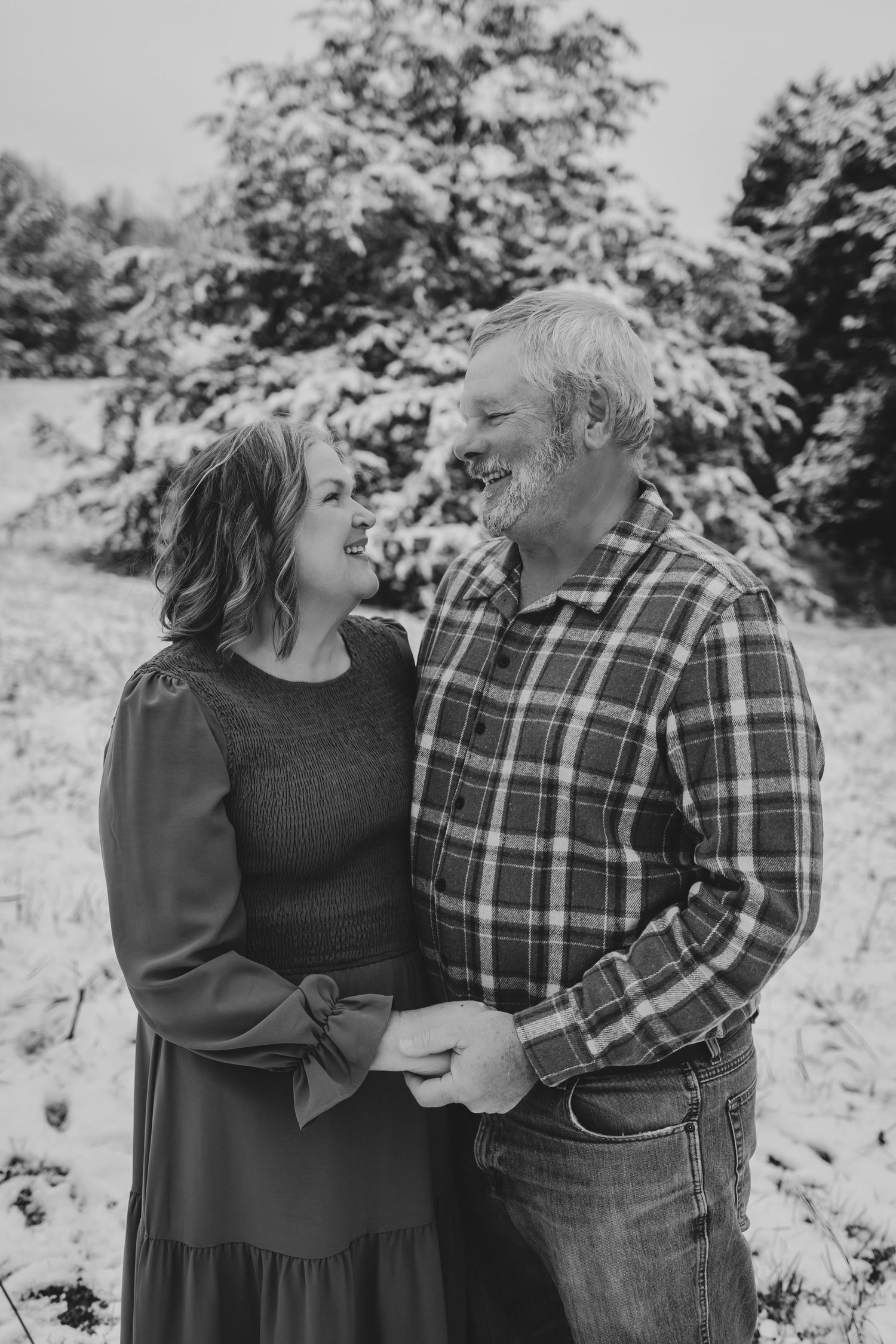 Couple laughing together in a snowy winter landscape wearing casual clothing.