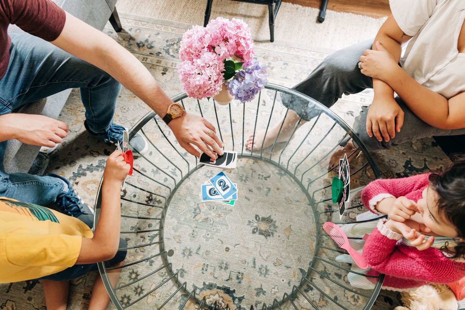 People gathered around a circular metal table with a vase of pink flowers having a relaxed social moment together playing UNO