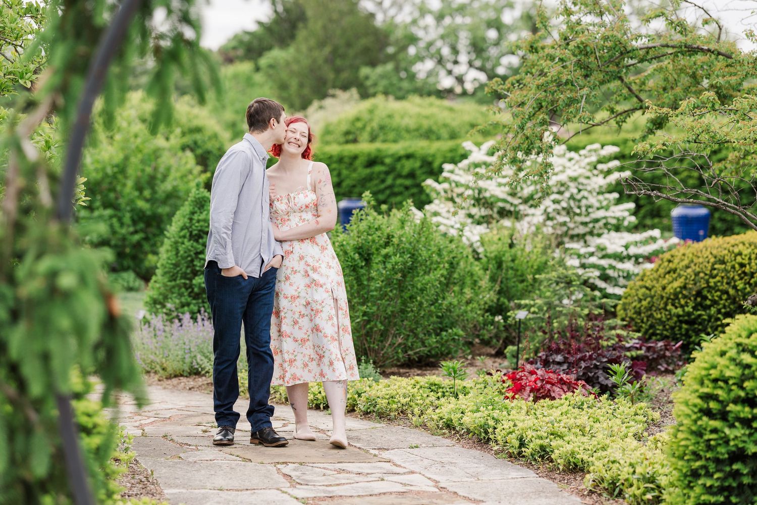 A couple walks together on a stone path surrounded by lush summer gardens and flowering shrubs at Cantigny Park