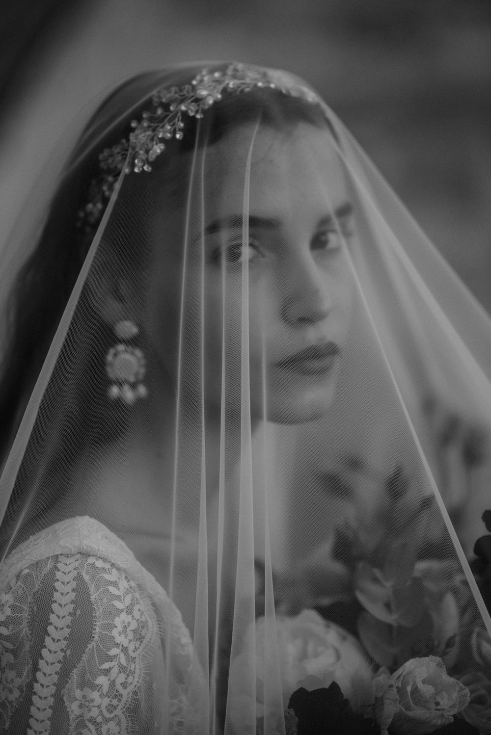 Artistic bridal portrait through delicate veil with intricate headpiece and lace details.