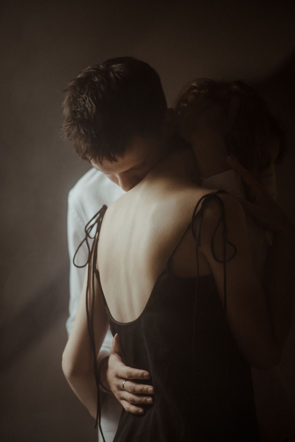 Intimate moody portrait in bed with tender embrace in dark atmospheric lighting. Romantic couple photoshoot.