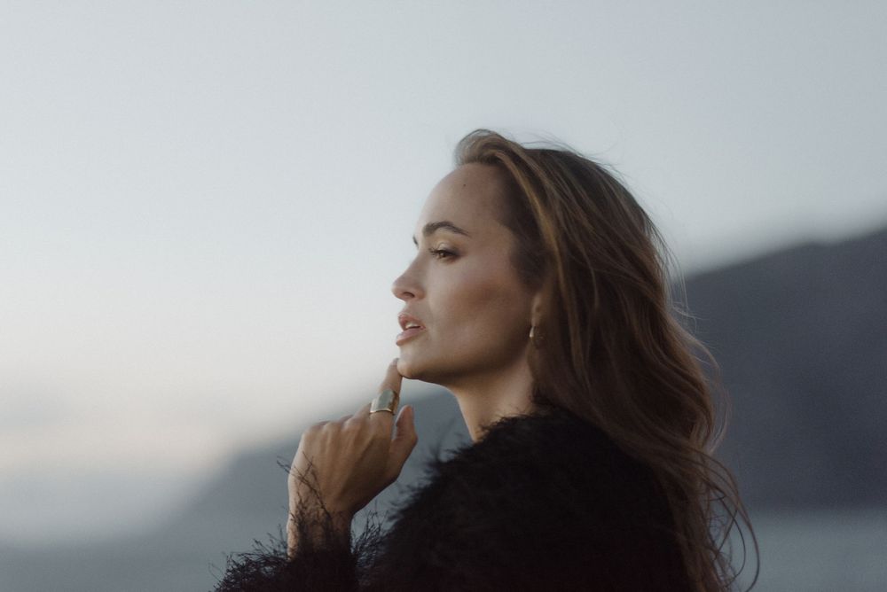 A person with flowing hair gazes thoughtfully into the distance at dusk against a misty mountain backdrop of Los Gigantes.