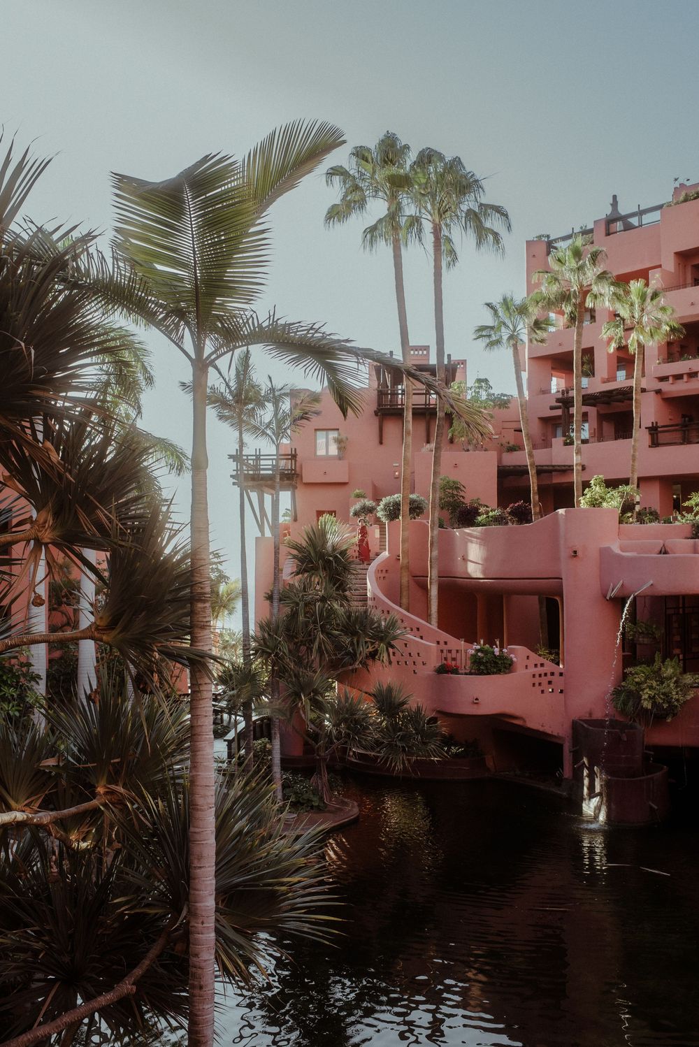 A pink resort building of Ritz-Carlton Abama with cascading balconies surrounded by palm trees and reflecting pools in a tropical setting