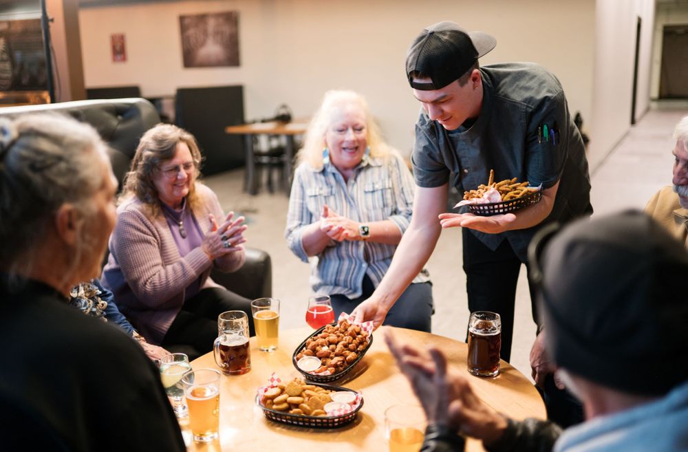 A server bringing plates of food to a group gathered around a table.