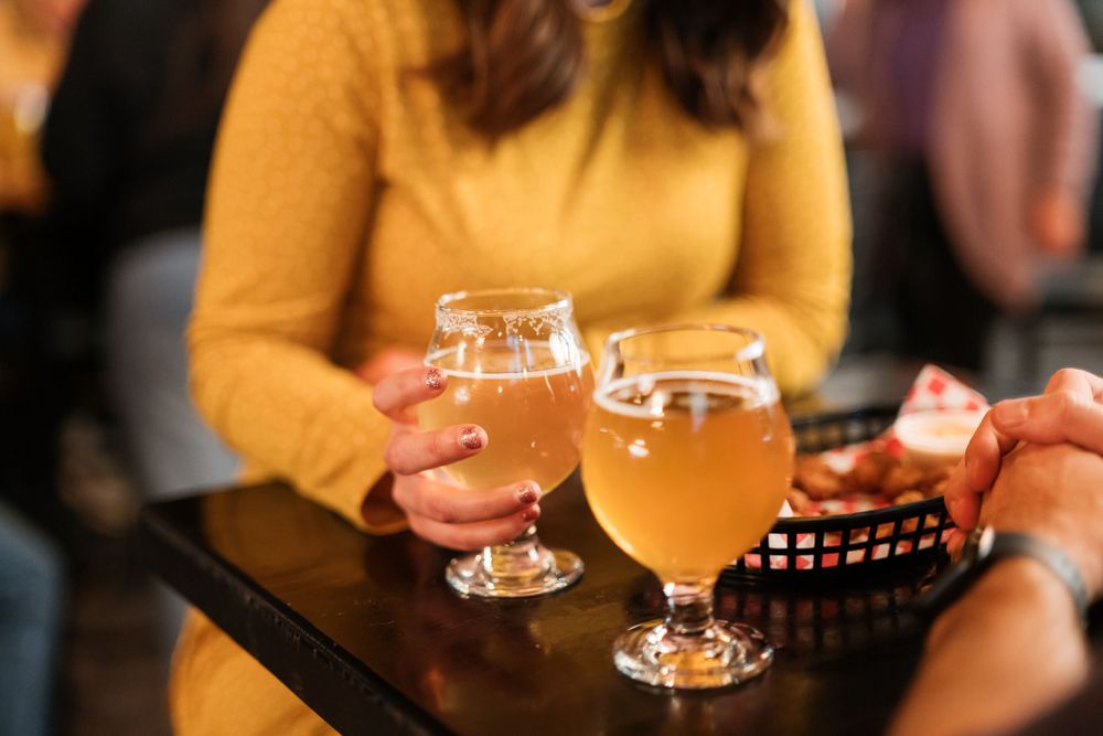 Two glasses of craft beer on a dark wooden table at a bar.
