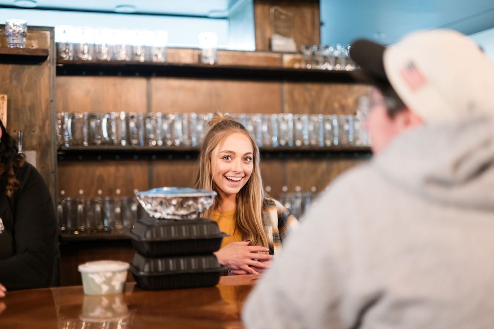 Casual conversation at a bar with glassware displayed on shelves in background.