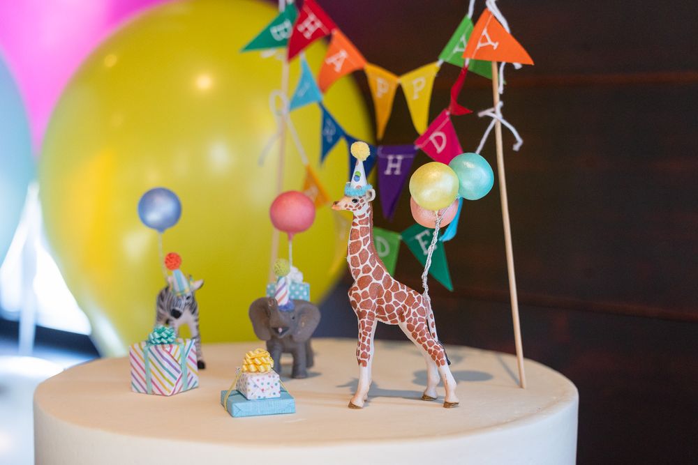Safari animal figurines arranged on cake stand with colorful birthday bunting.