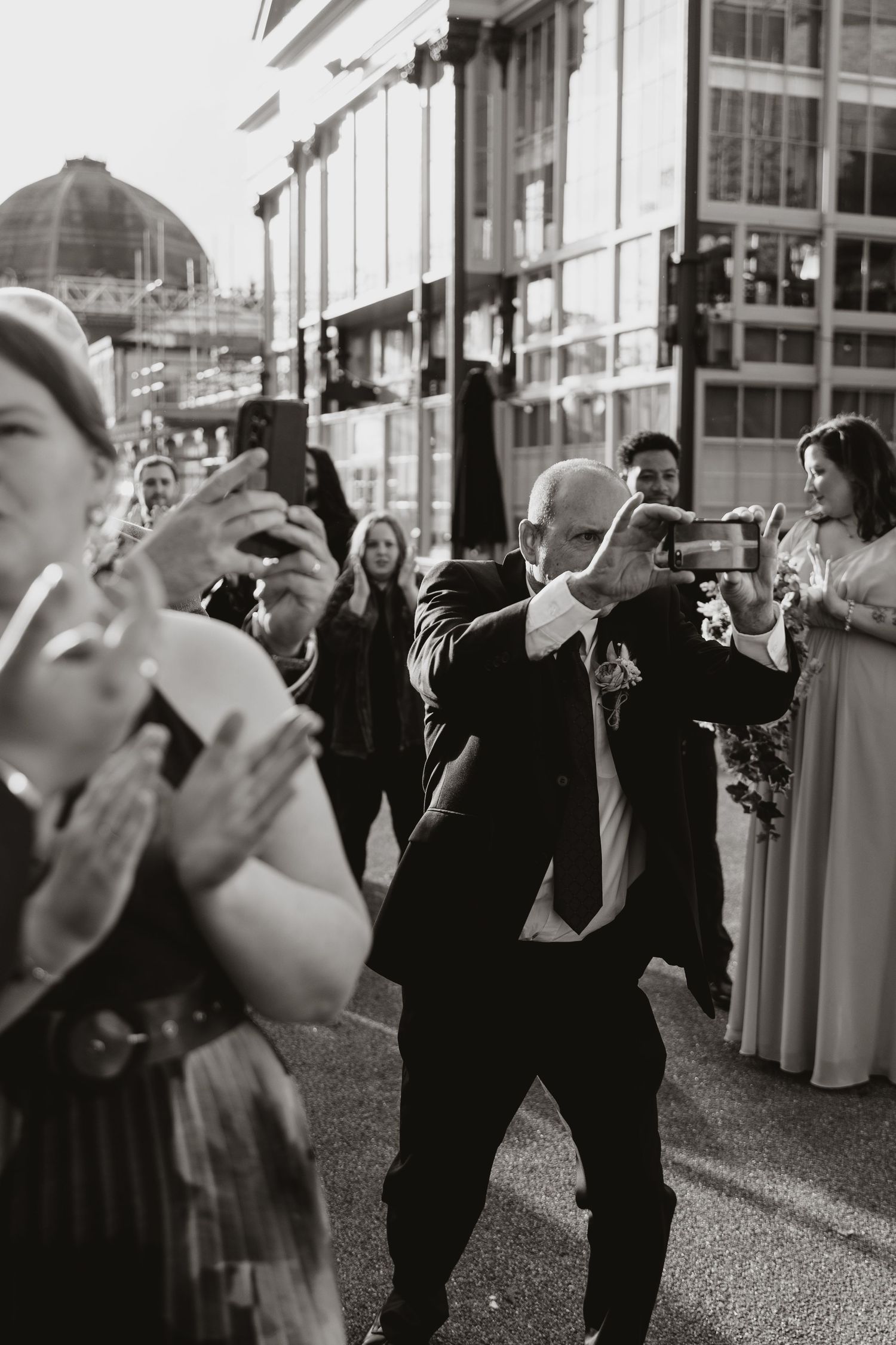 A person in a dark suit taking a photo of bride at a wedding while others look on.