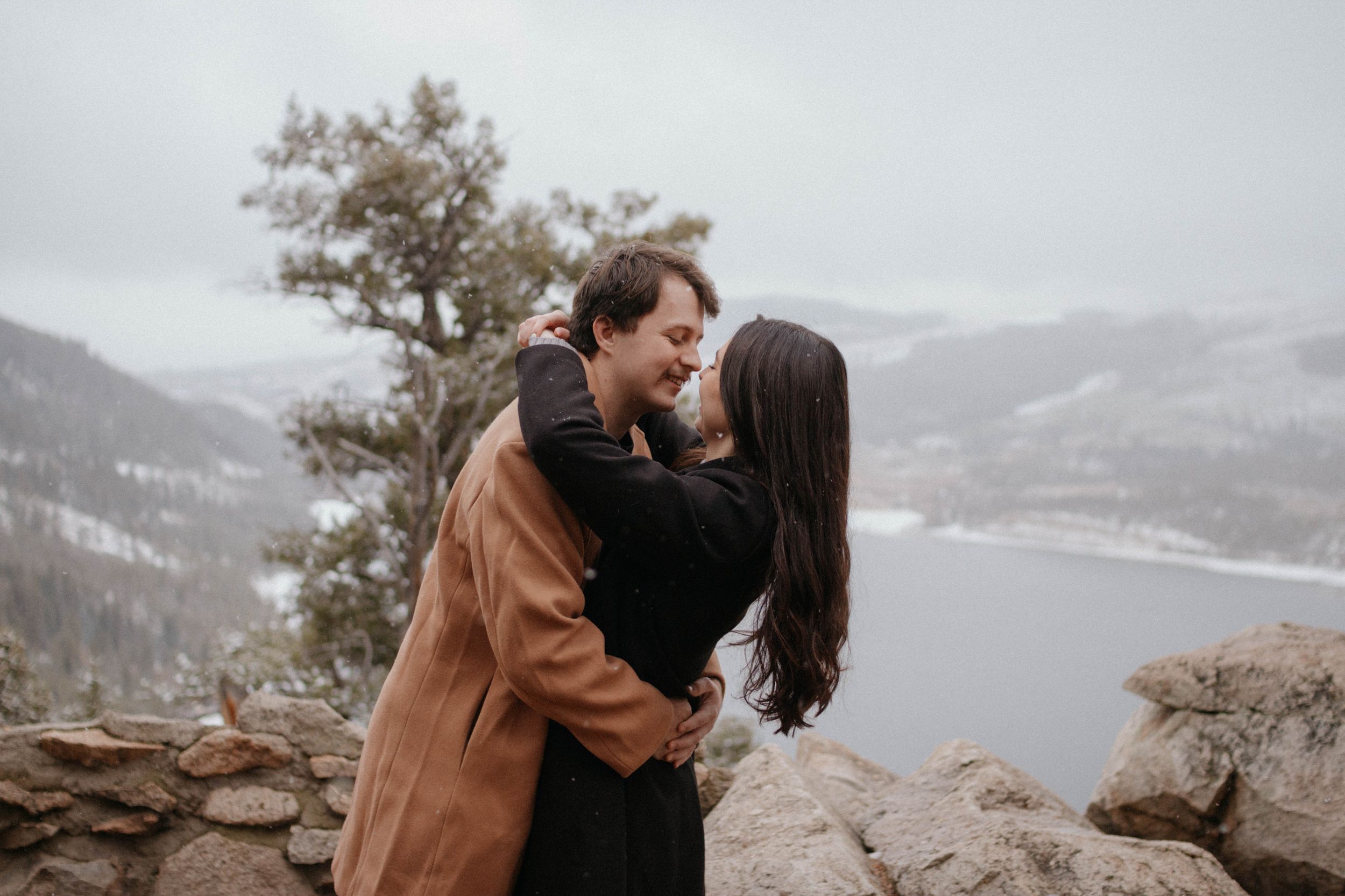 engagement photoshoot, couple in warm winter coats standing on a winter lake and mountains background. Breckenridge, Colorado
