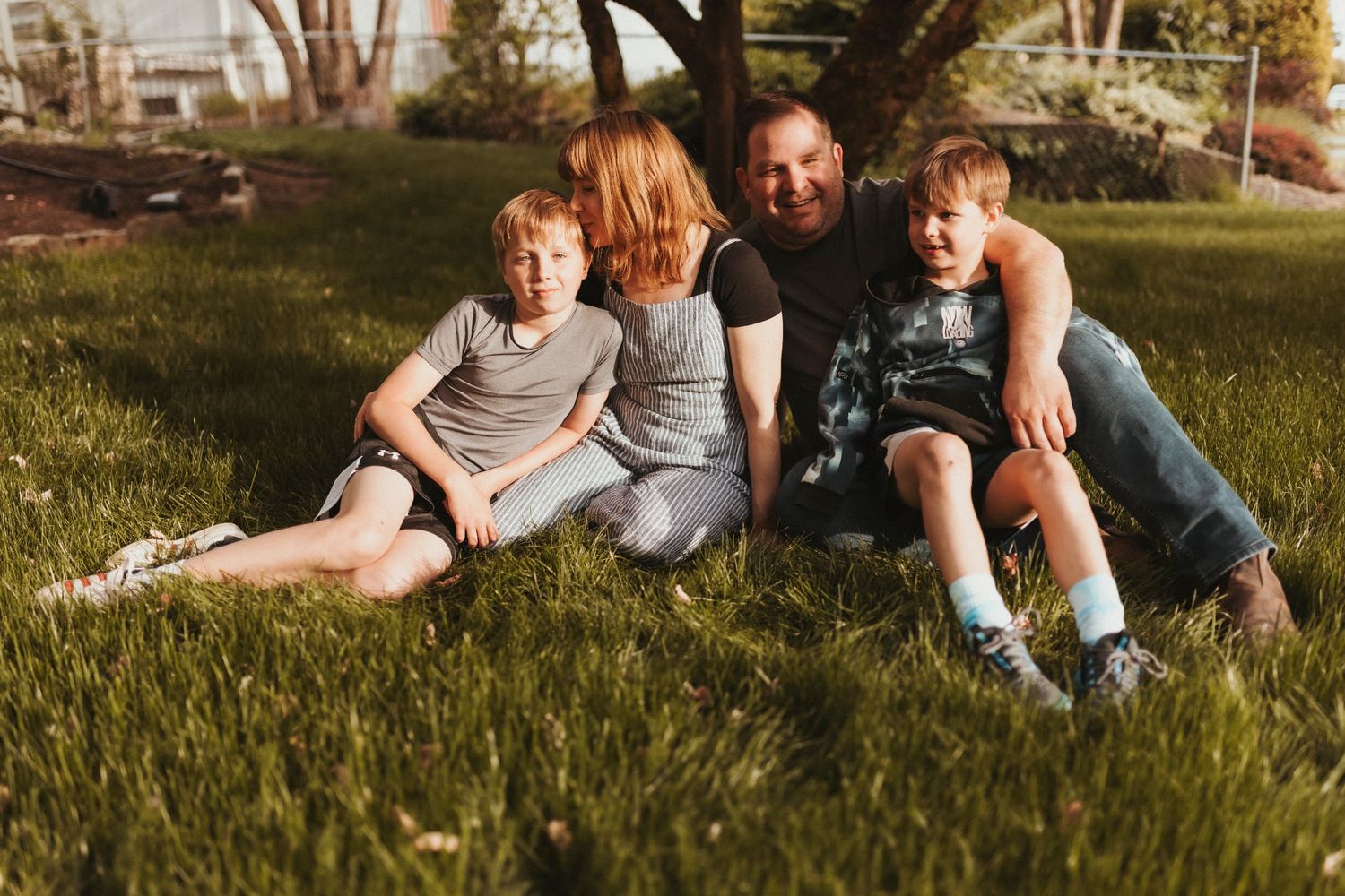 a family sit together on the front lawn. They hug and laugh while the sun goes down. Elizabeth Lang Photography Surrey