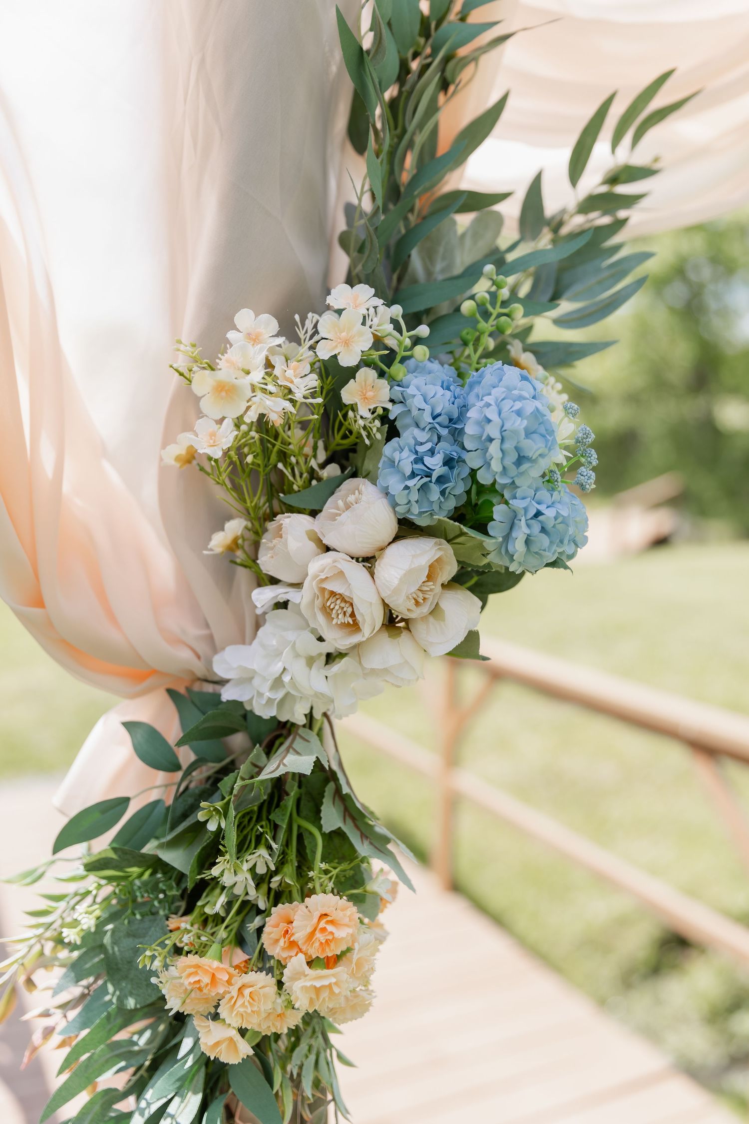 Beautiful floral arrangement with blue hydrangeas, white peonies, peach roses and greenery against a soft blush backdrop.