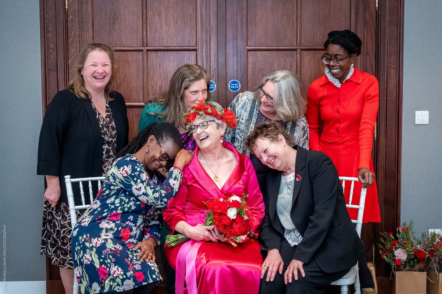 A group of people share laughter and joy while gathered together wearing formal attire with a bright red accent.