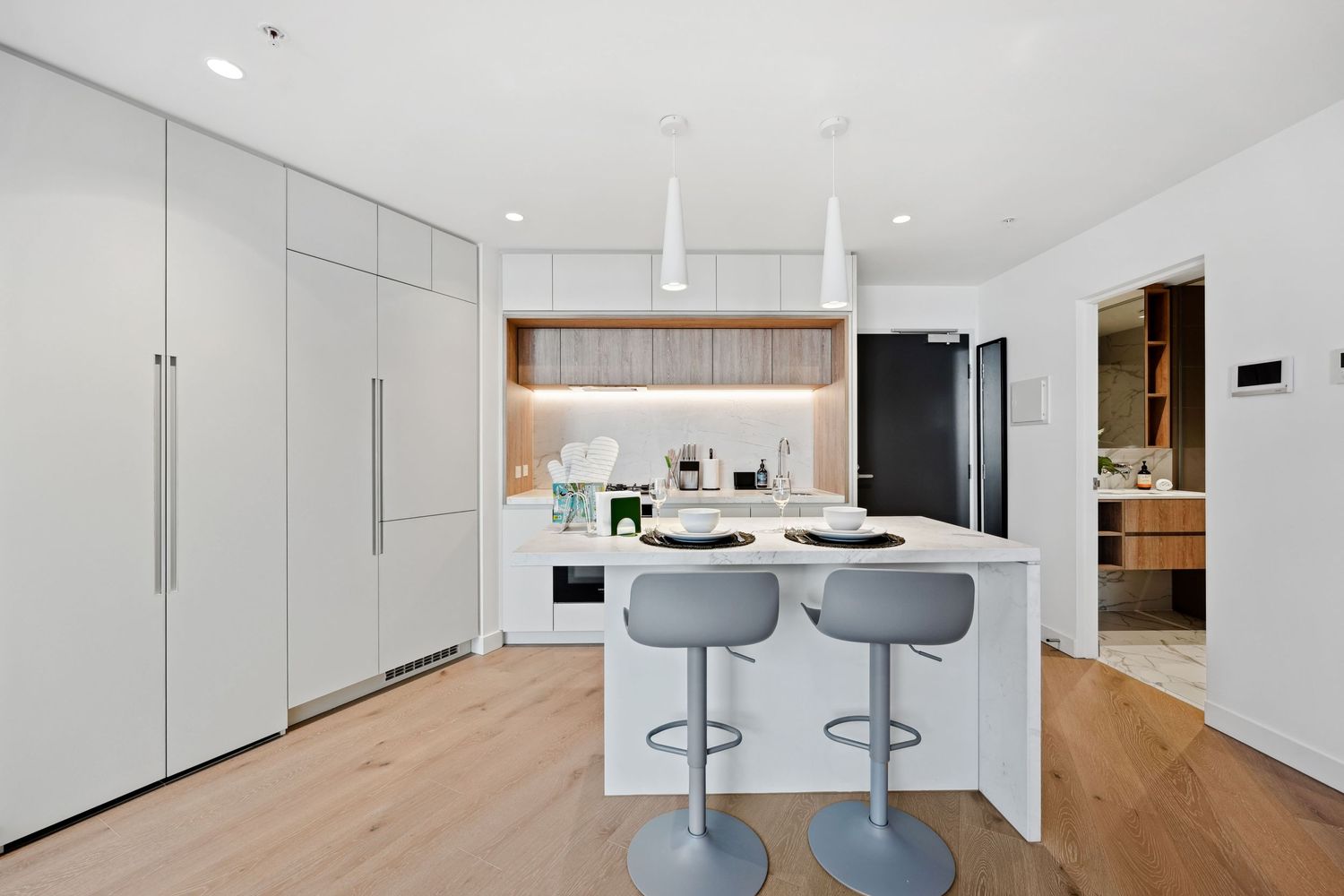 Minimalist white kitchen with custom cabinetry, island bar seating, and light wood flooring in contemporary style.
