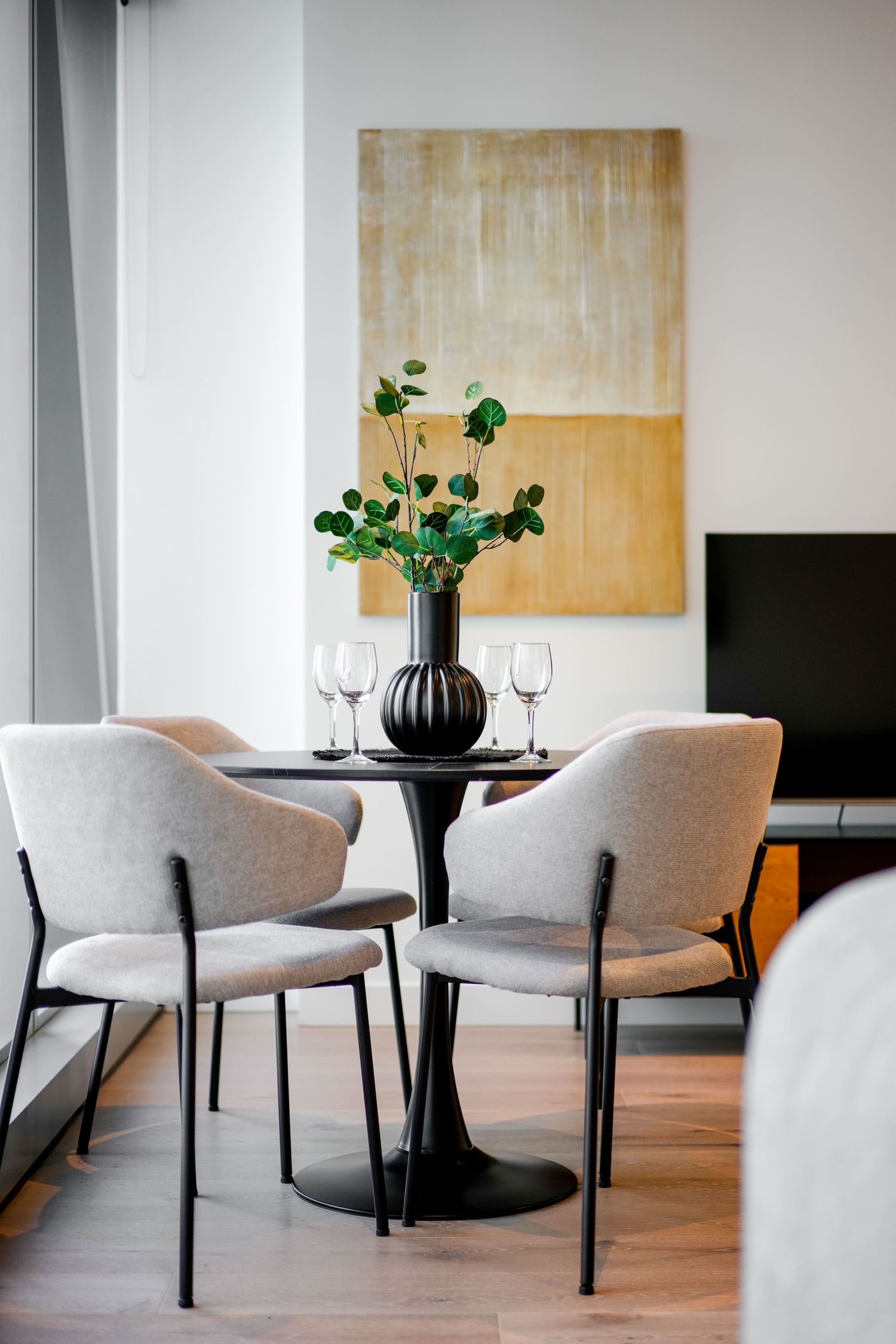 Modern dining nook with gray upholstered chairs, black tulip table, and abstract beige artwork on wall.