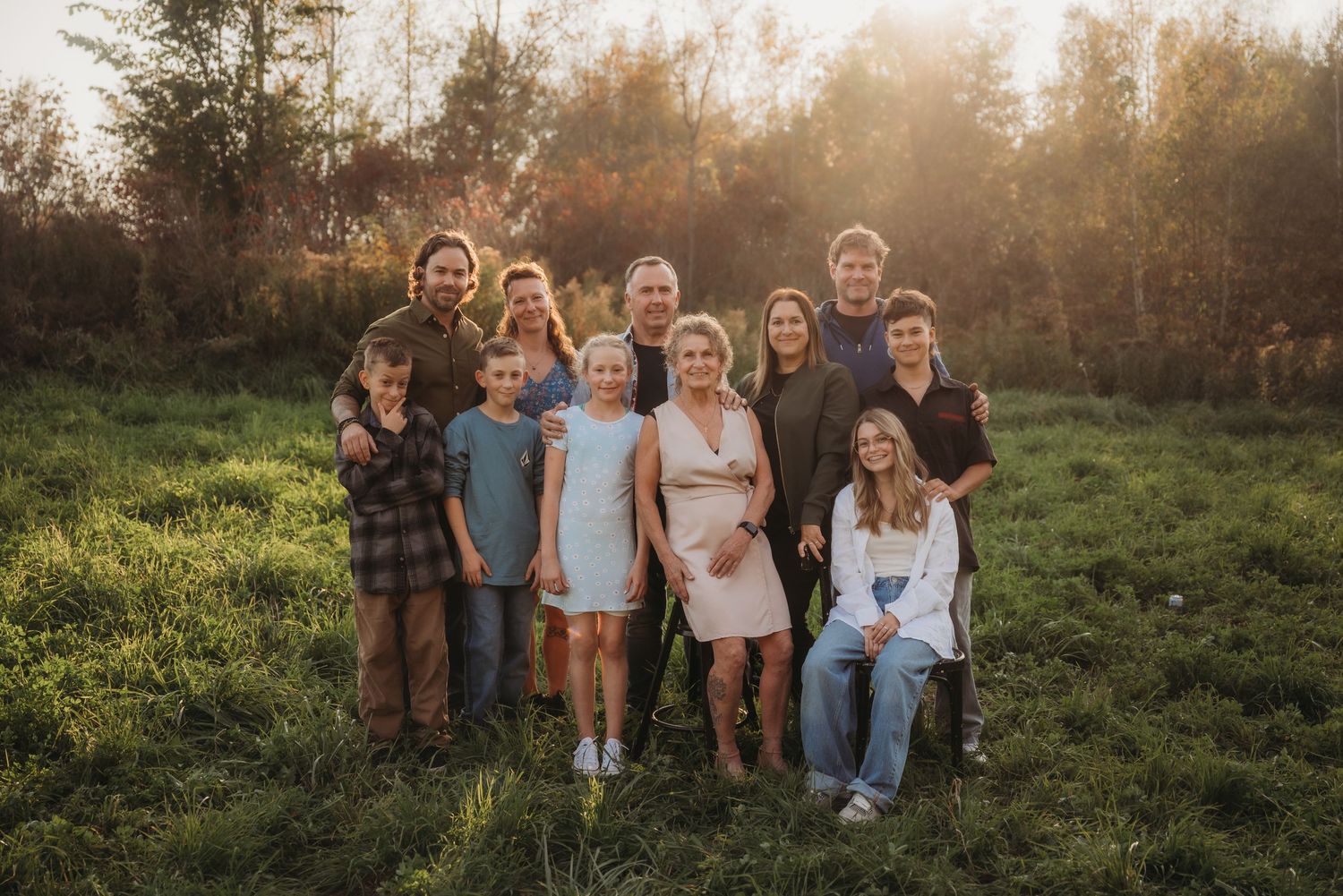 Large family group poses together outdoors in a grassy field during golden hour.